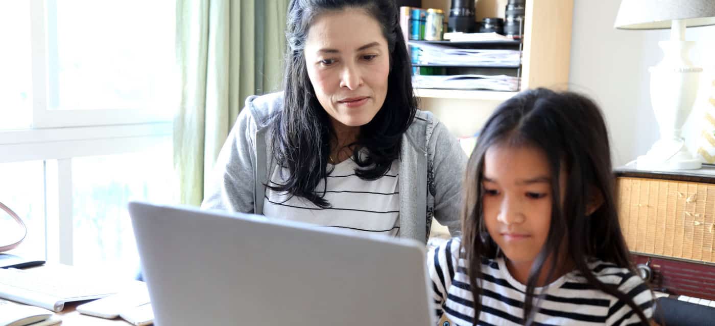 A woman and a young girl sitting at a table and using a laptop.