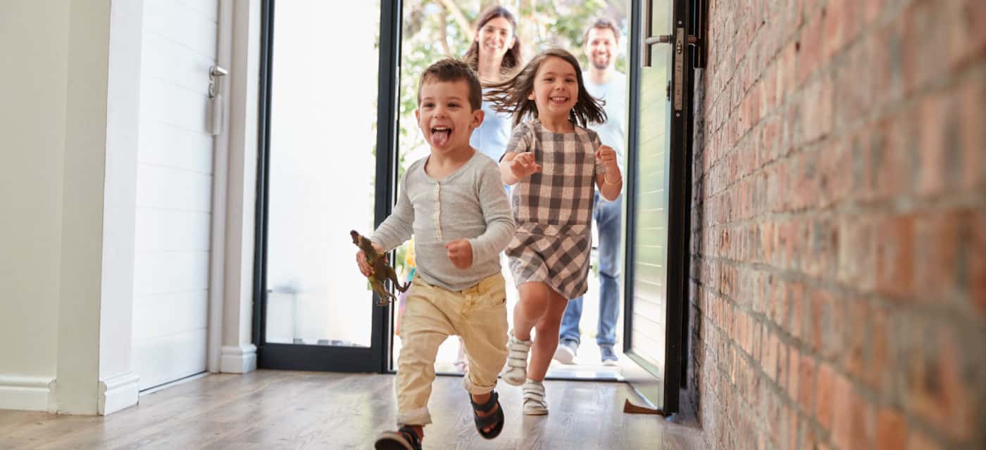 Kids running through the front door and into a house. Their parents are smiling behind them.