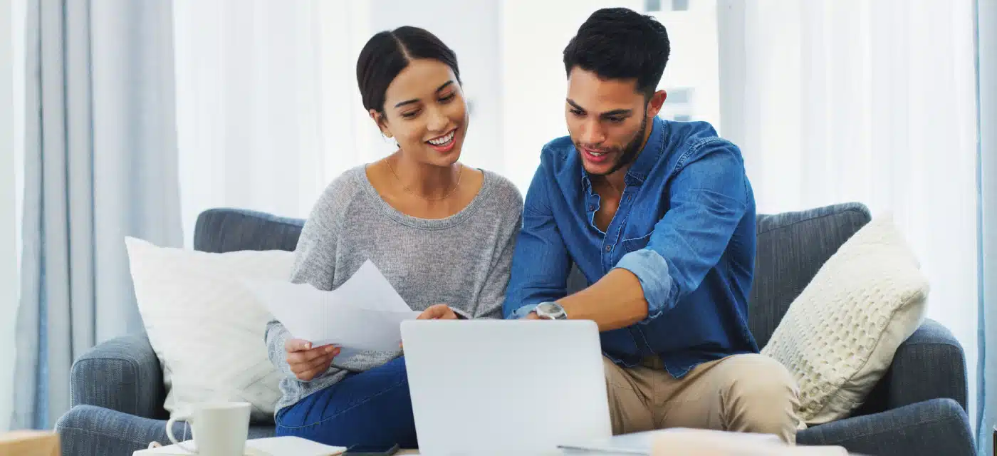 Two people look at laptop screen with papers in hand