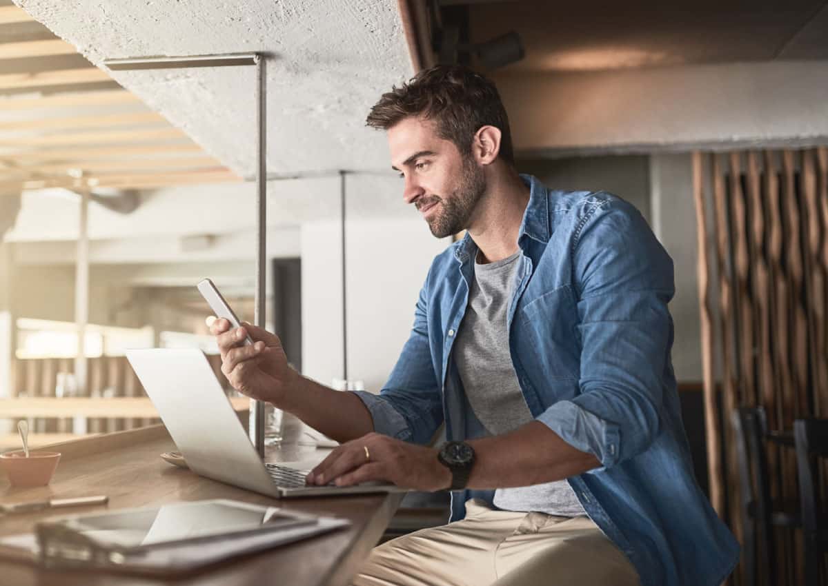 a man sitting at a table with a laptop open and using a cell phone.