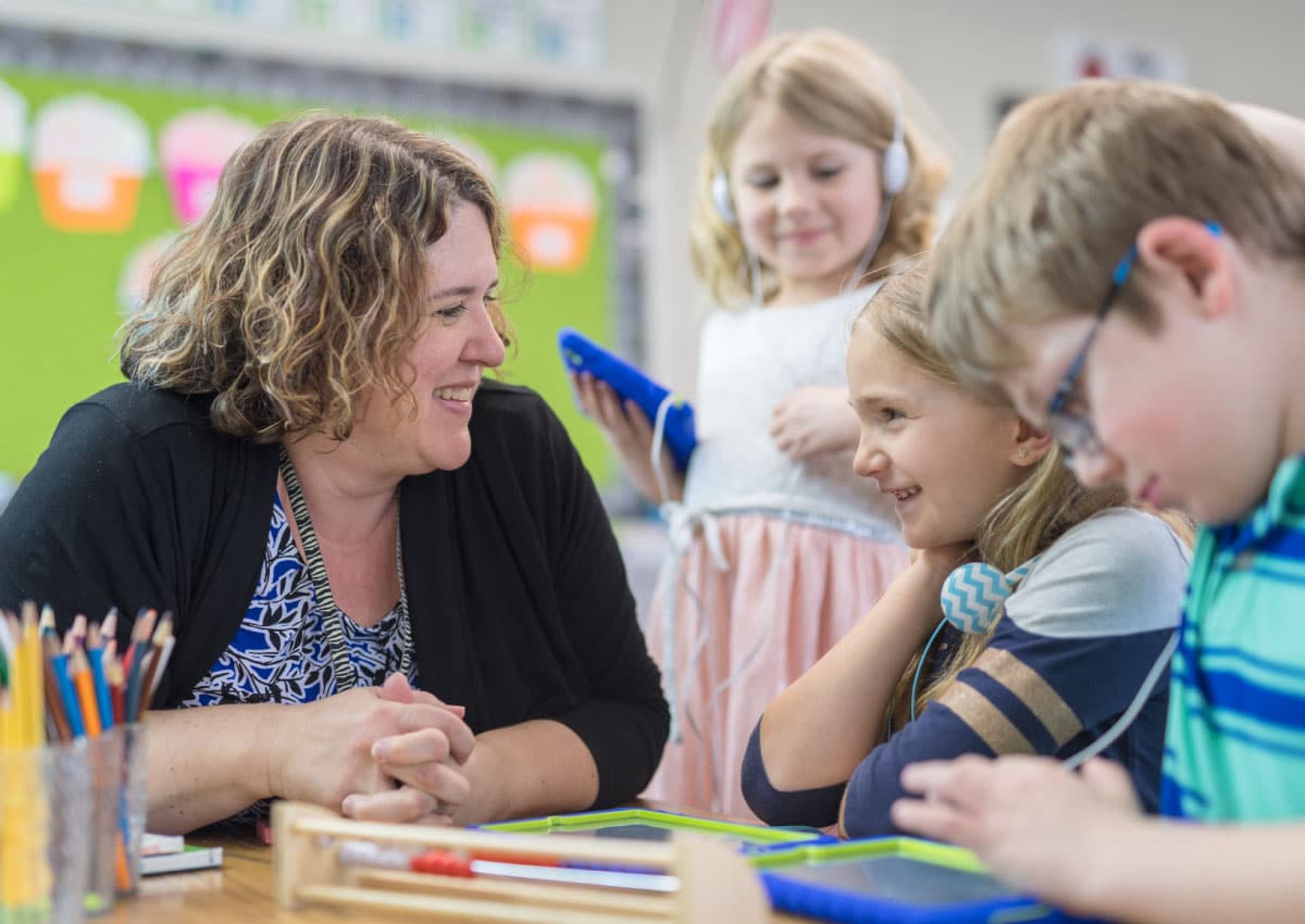 A woman sitting at a desk with a group of young children.