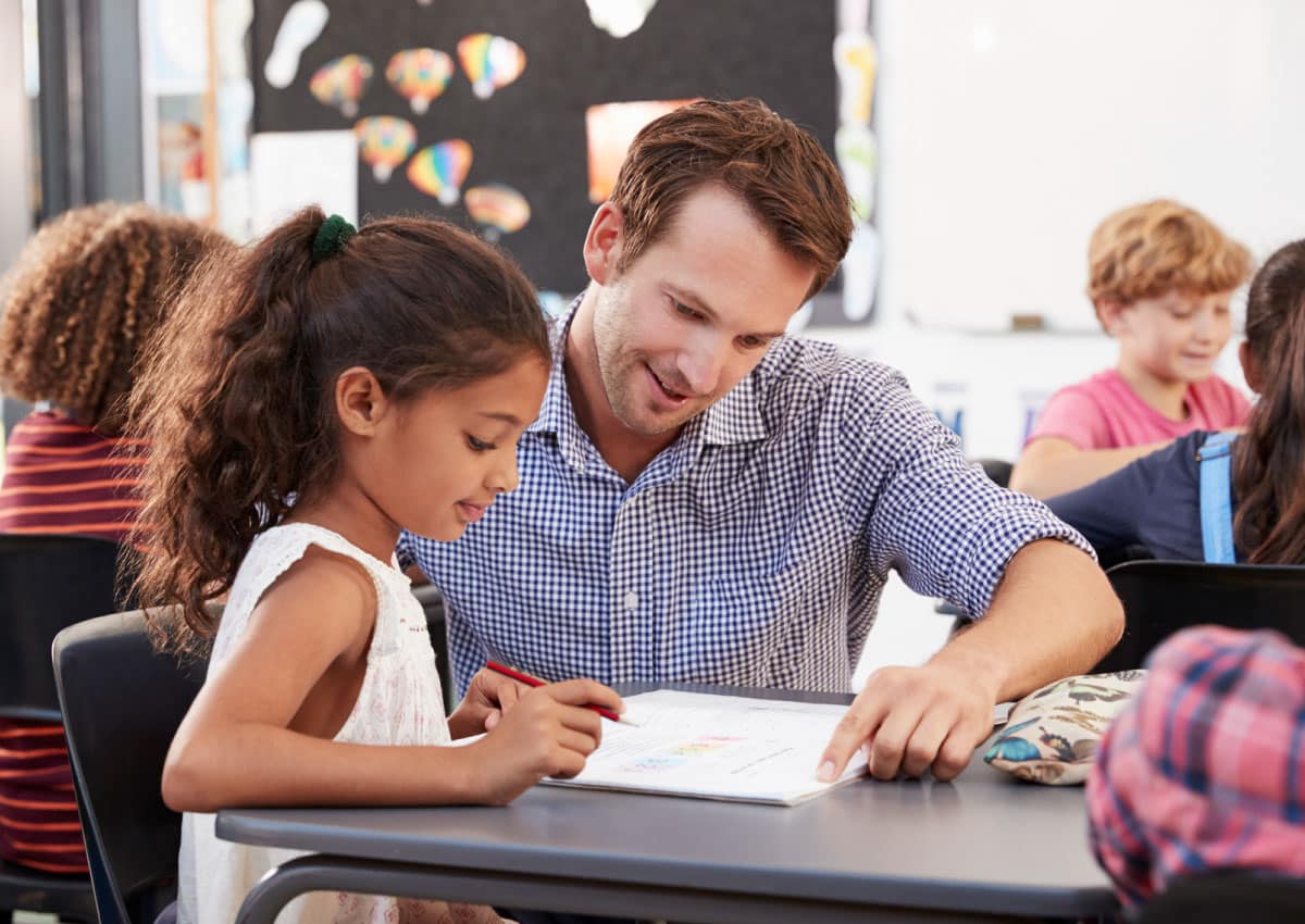 A man helps a young girl write something in a notebook.