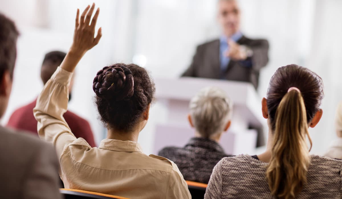 A woman raising her hand in class, the professor calls on her.