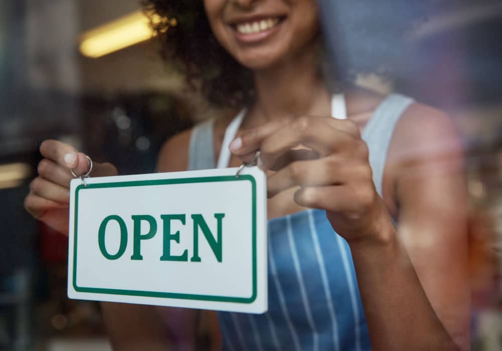 A woman putting a sign in a window that reads "open"