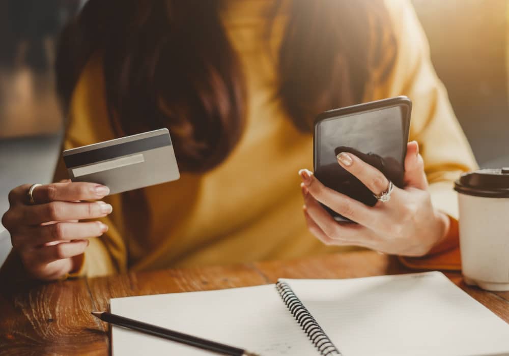 A woman holding a cell phone and a credit card.