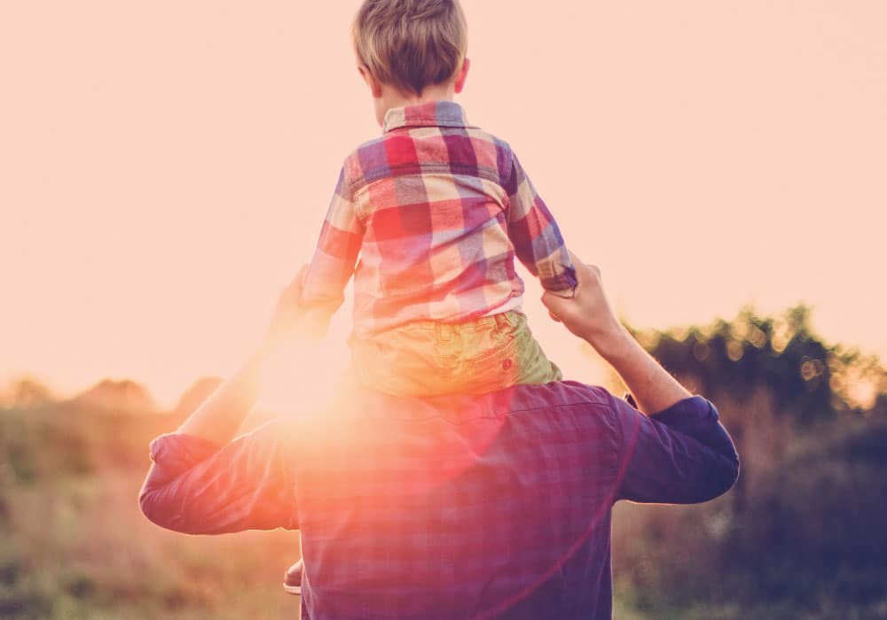 Child sits on parent’s shoulders while outside