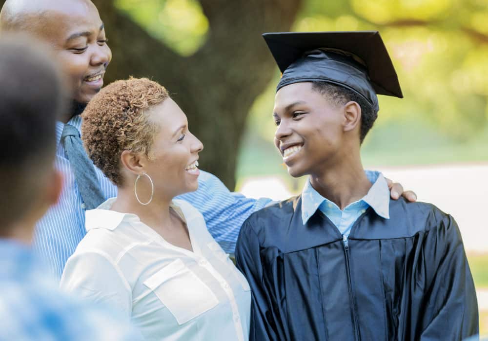 A young boy in a graduation cap smiles at two adults.