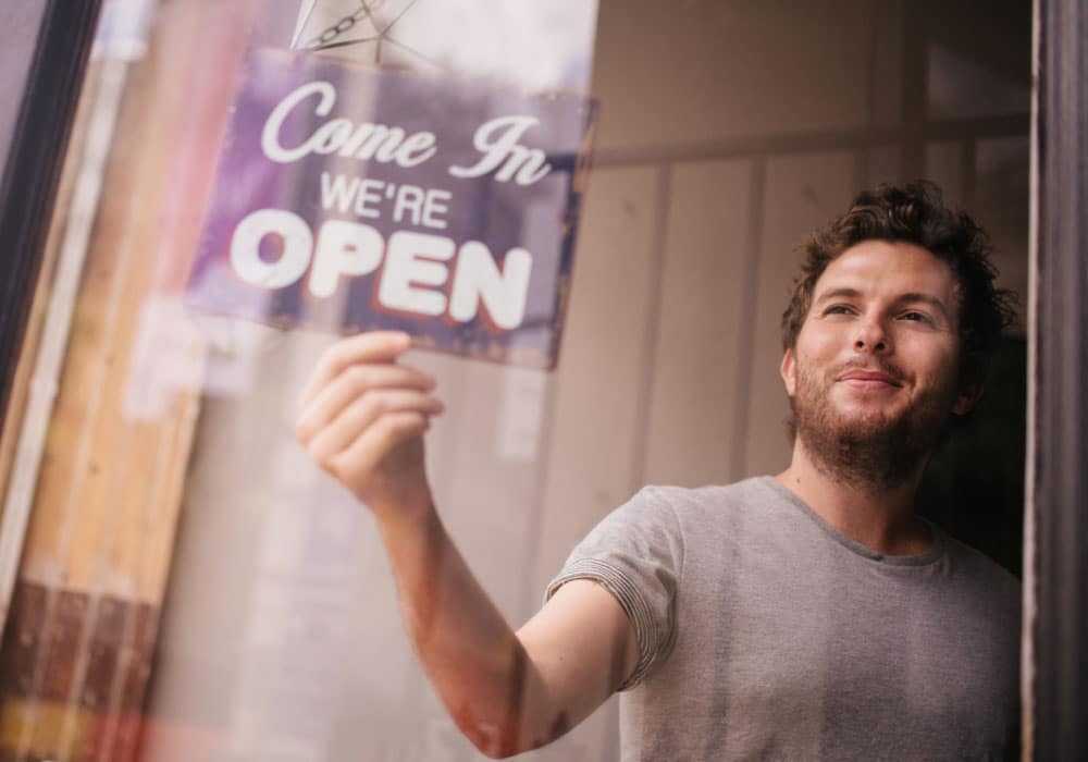 A man puts a sign in a window that says "we are open"