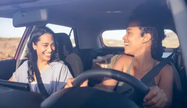 Two women in a car look at each other while laughing.