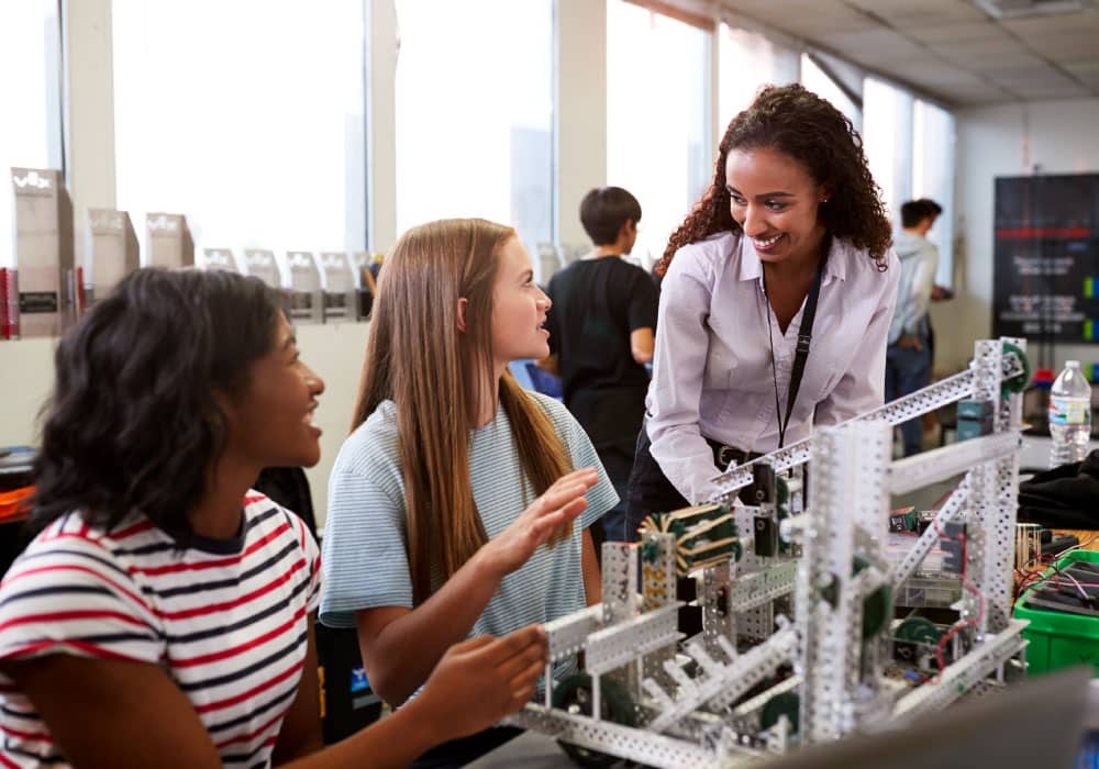 A woman with two high school age kids, there is a robot on the table in front of them.