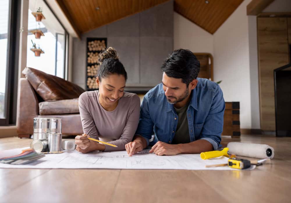 A couple sits on the floor looking at blueprints.