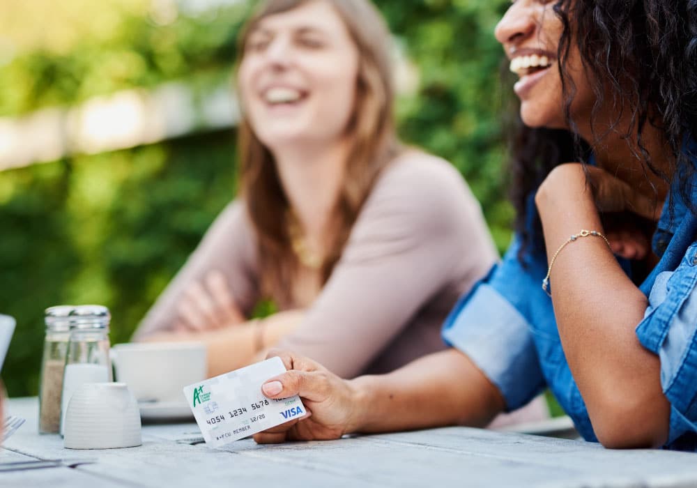 A woman holding an A+FCU debt card.