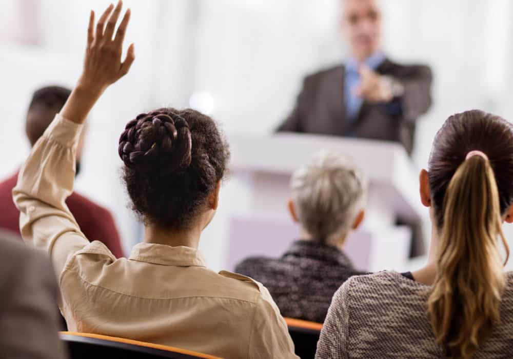 A woman raising her hand and being called upon in a classroom setting.