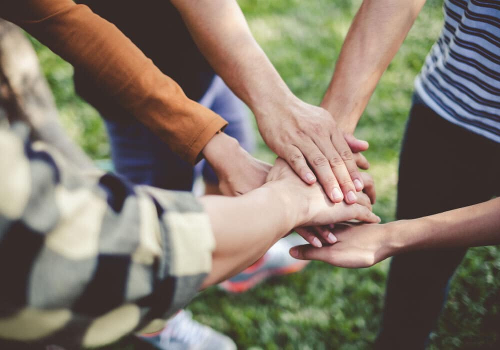 a group of people in a circle with their hands in the middle.