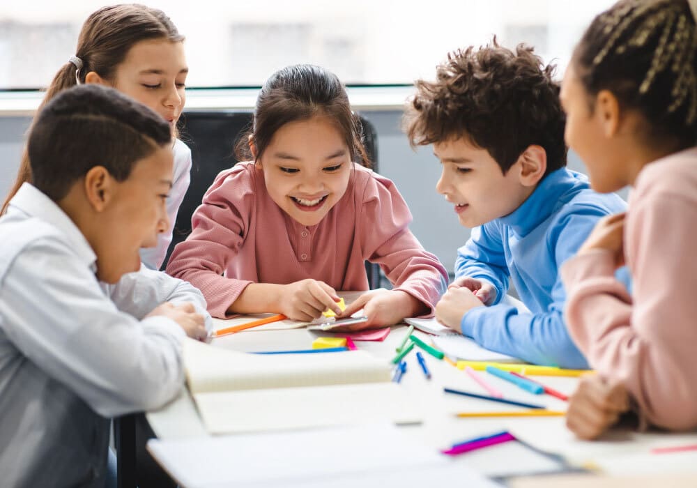 A group of kids sitting around a table with a bunch of colored markers.