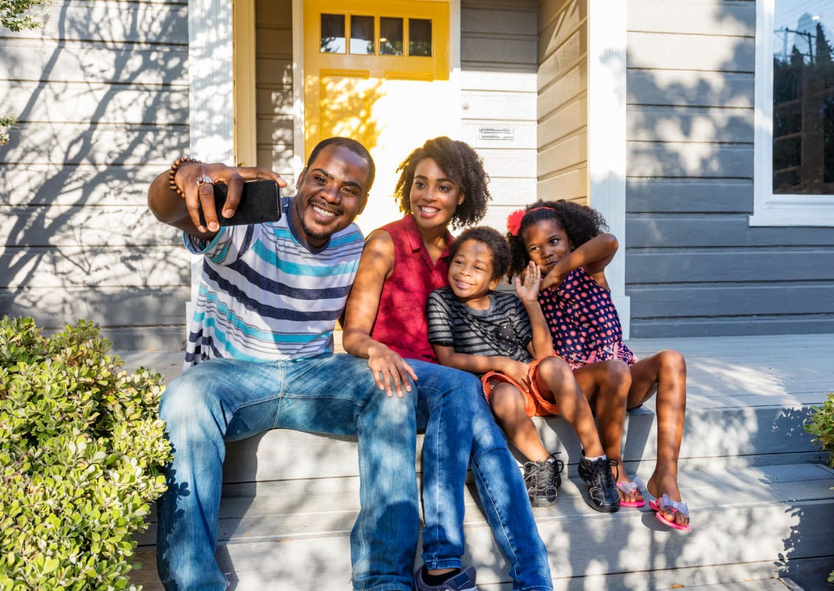 A family of four, taking a selfie on the front porch of their home.