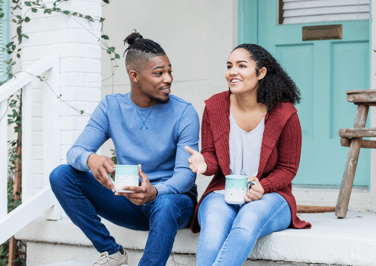 A young man and young woman sitting on a porch talking.