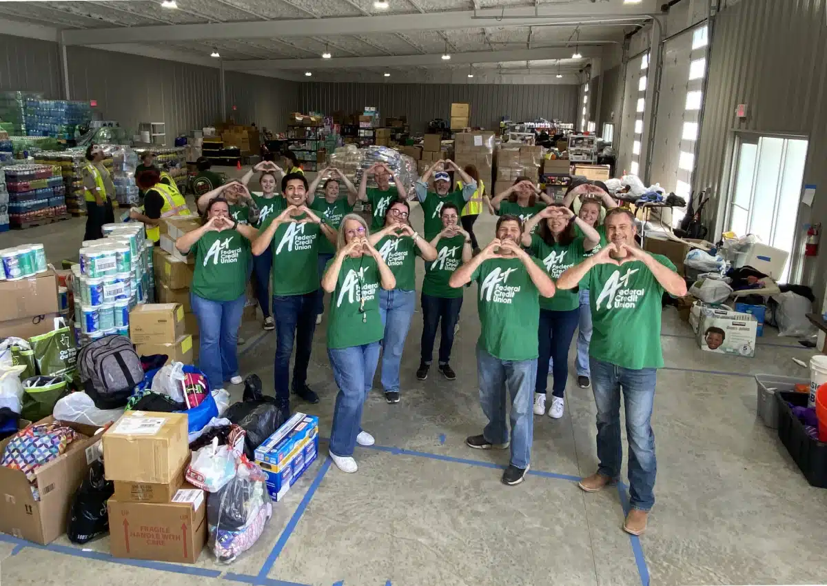 A+FCU Team members wearing green shirts, standing together making hearts with their hands in front of donation boxes.