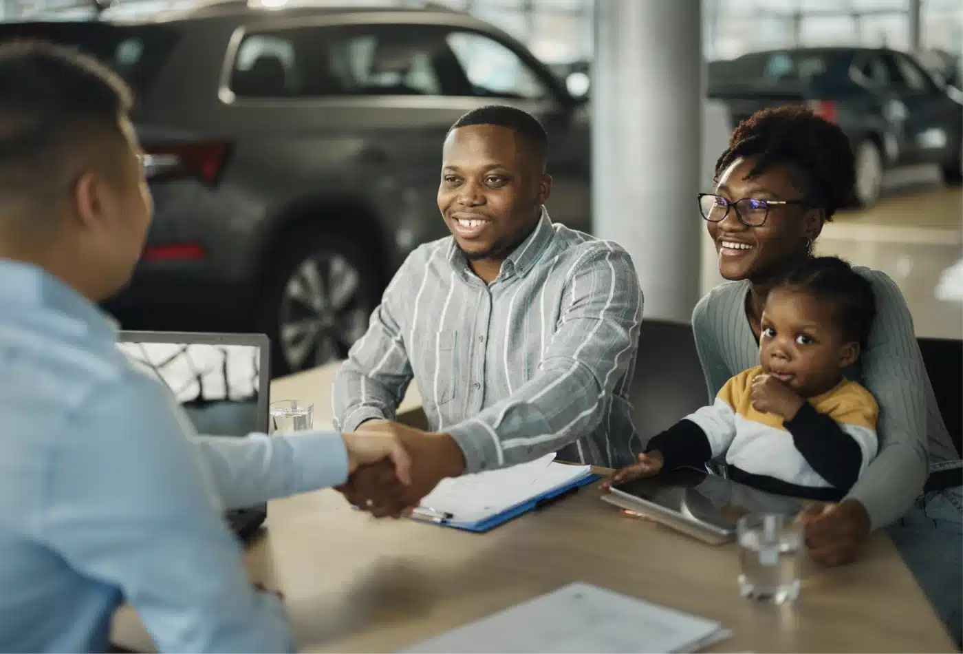 Man shaking hands with a car salesperson along with his family