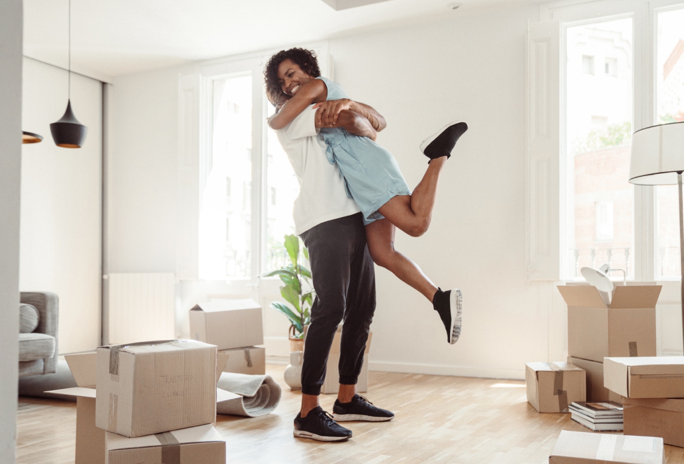 A man excitedly lifting a woman up in a living room of a new home.