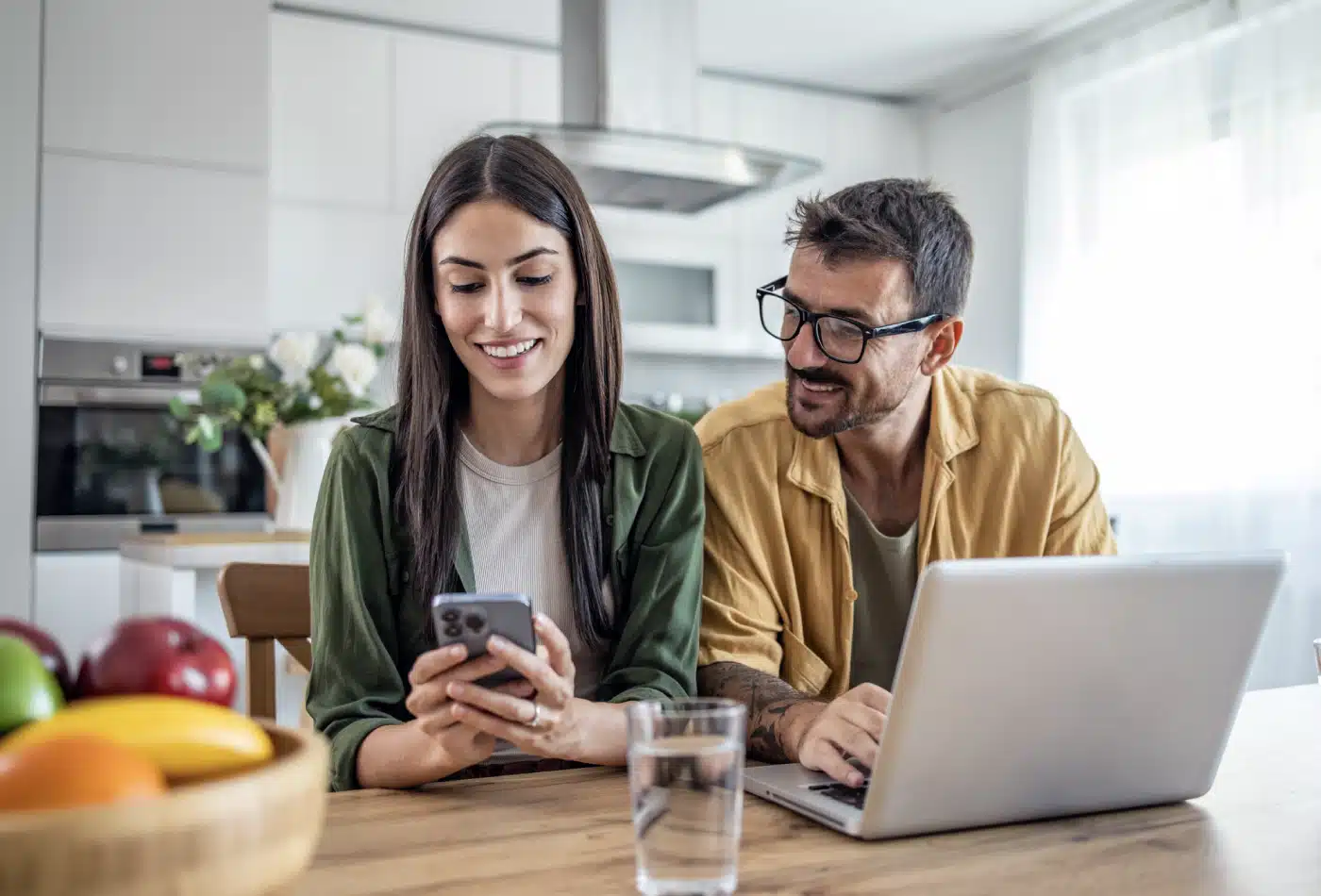 Man and woman sit at kitchen table with laptop and mobile phone.