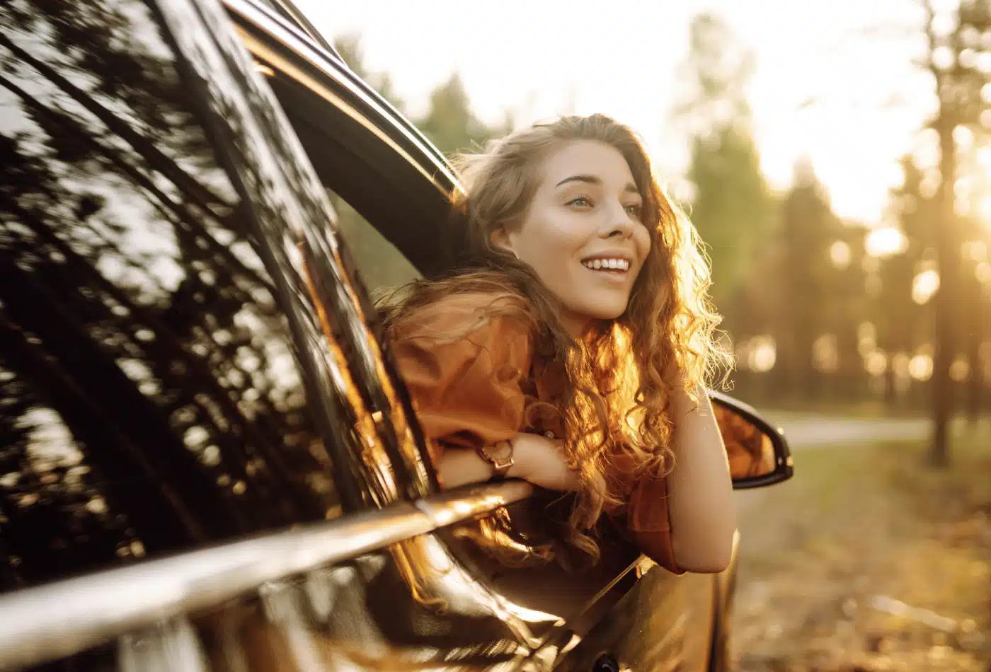 Woman leans out of a passenger side of the car smiling.