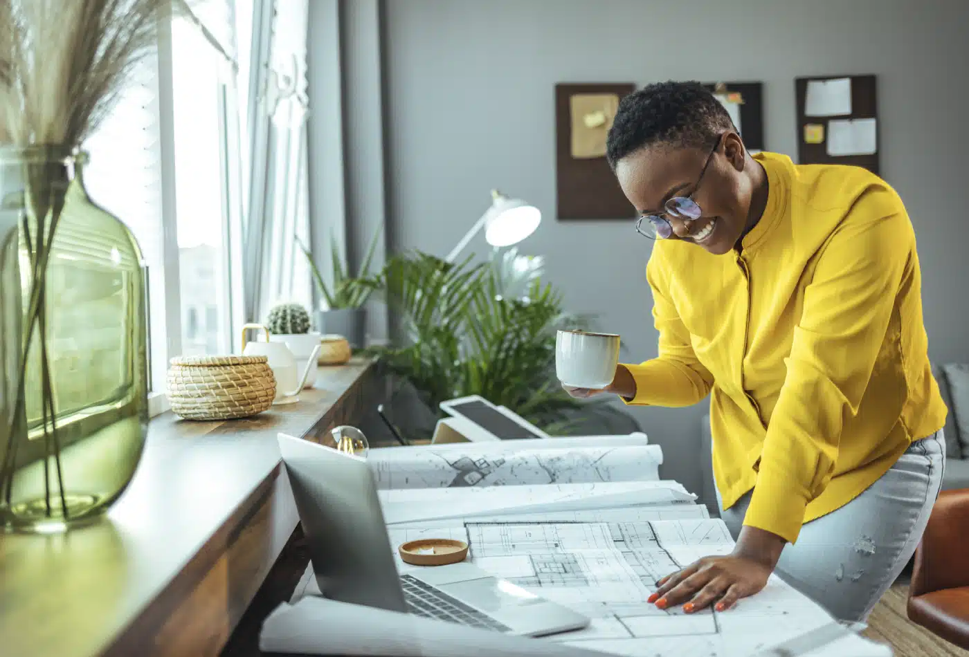 Woman holds coffee mug while leaning on table looking at blueprints