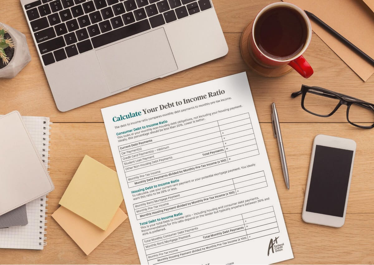 Printed copy of the debt-to-income worksheet on a desk with a laptop, phone, glasses, coffee.