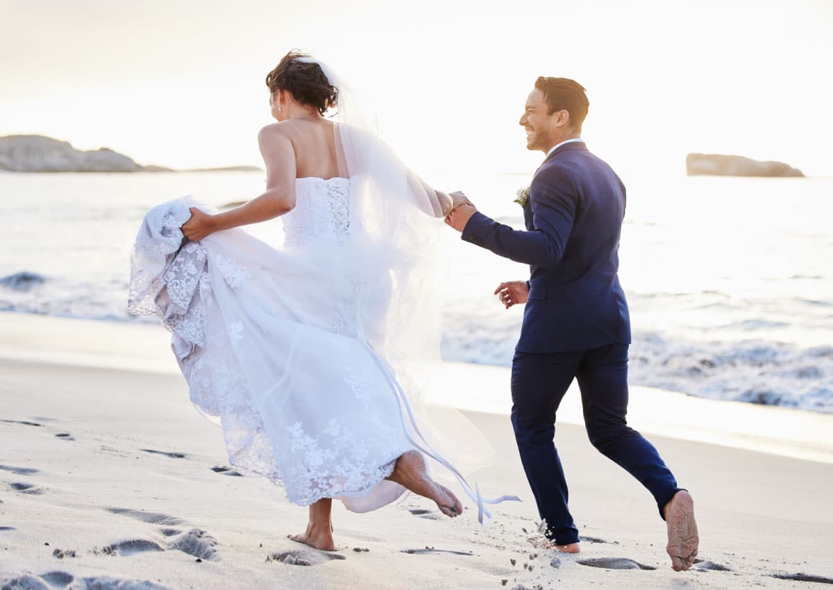 couple in wedding attire run across the beach