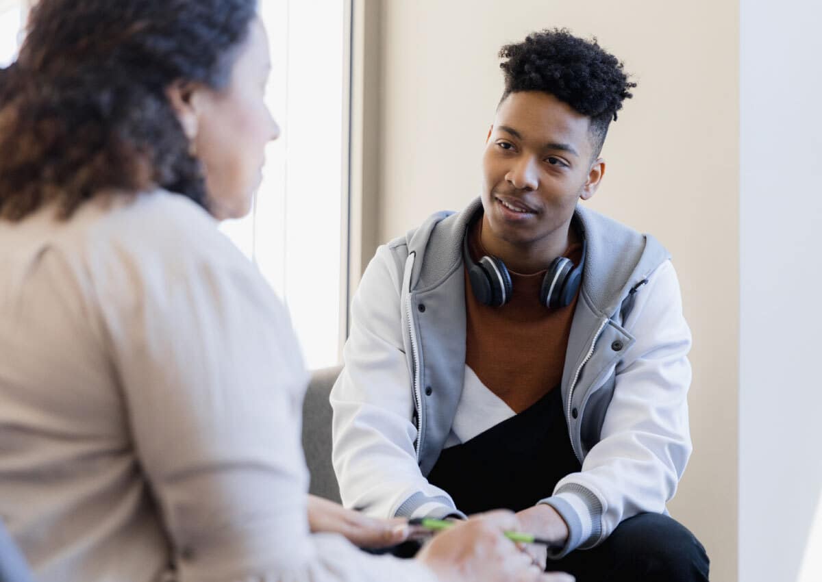 Young man is talking with older woman. Young man has headphones around neck.