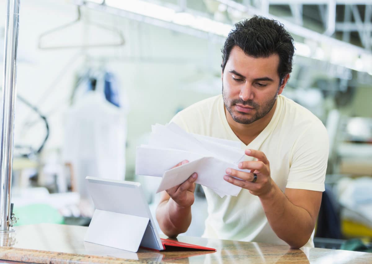 A man in front of a laptop looks through envelopes