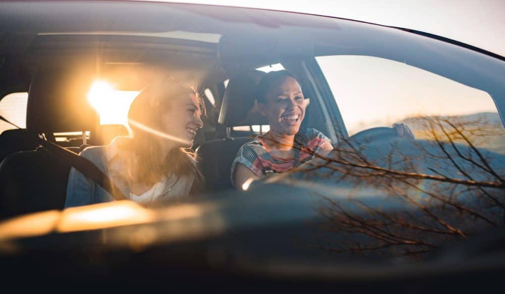 Two women driving a car and smiling.