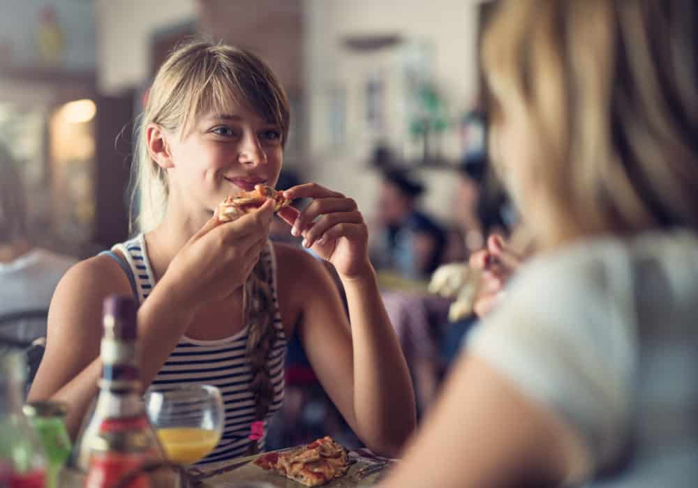 A teen sits at a table and eats a slice of pizza.