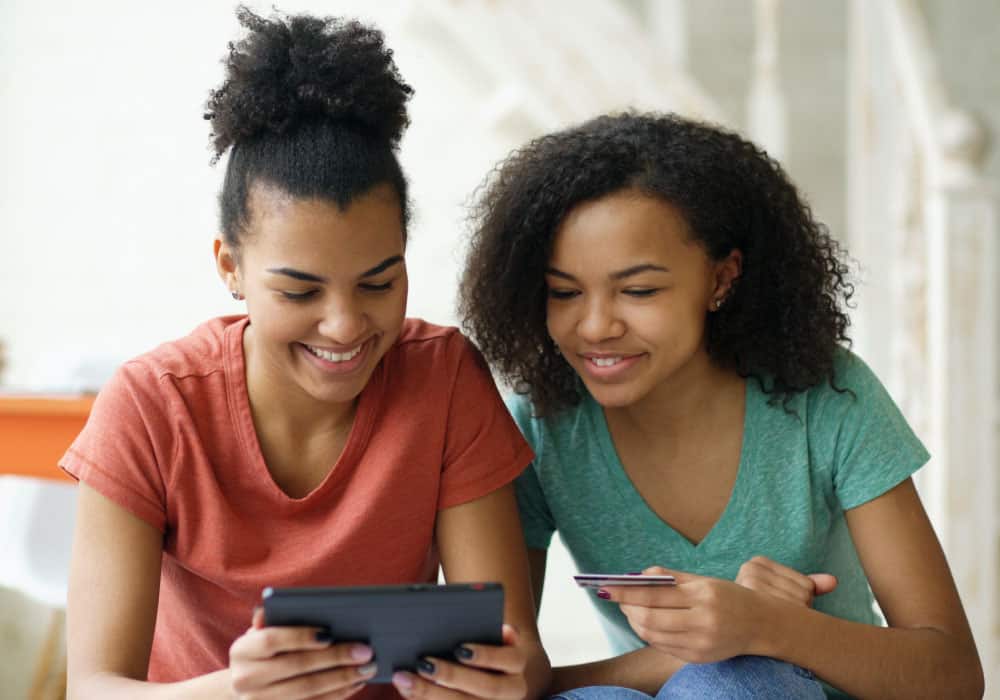two young girls looking at a tablet, one of them is holding a credit card.