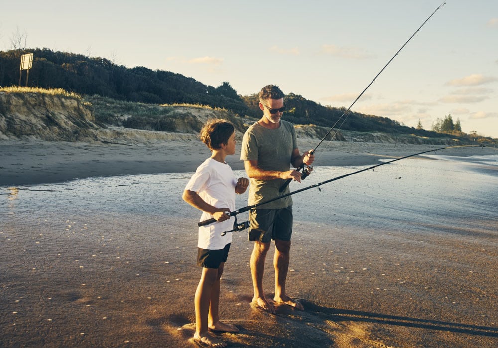 Father and son stand on beach with fishing poles