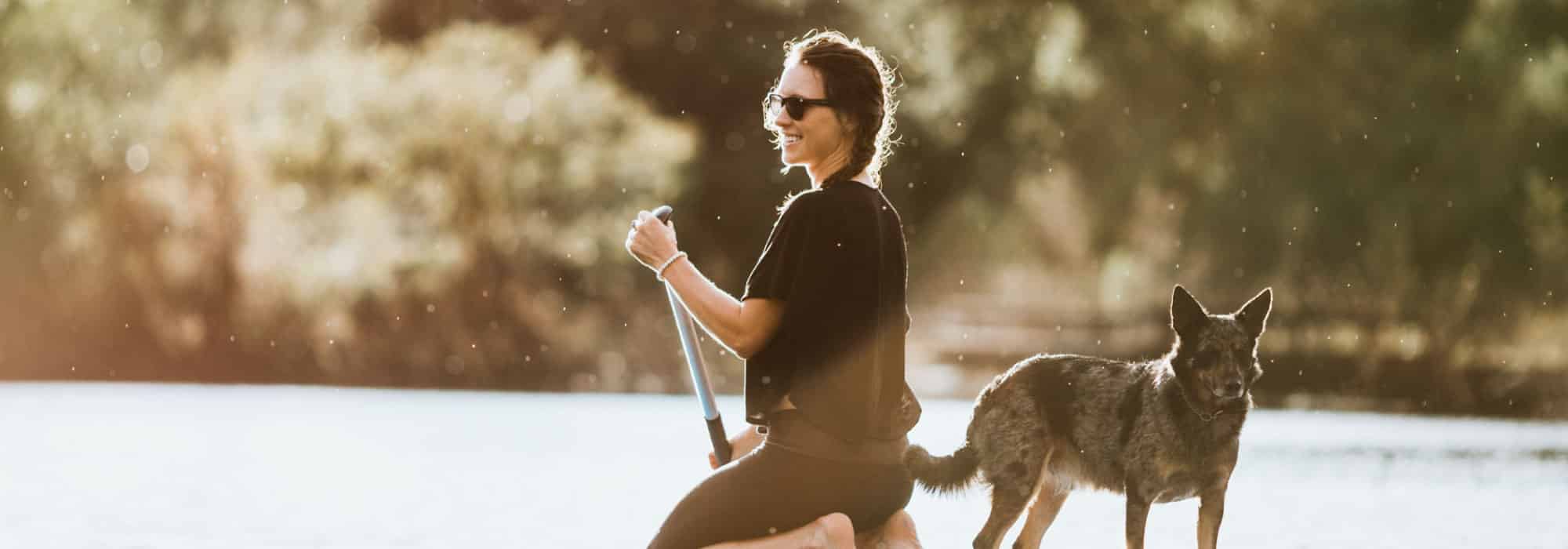 A woman on a paddle board with a dog.