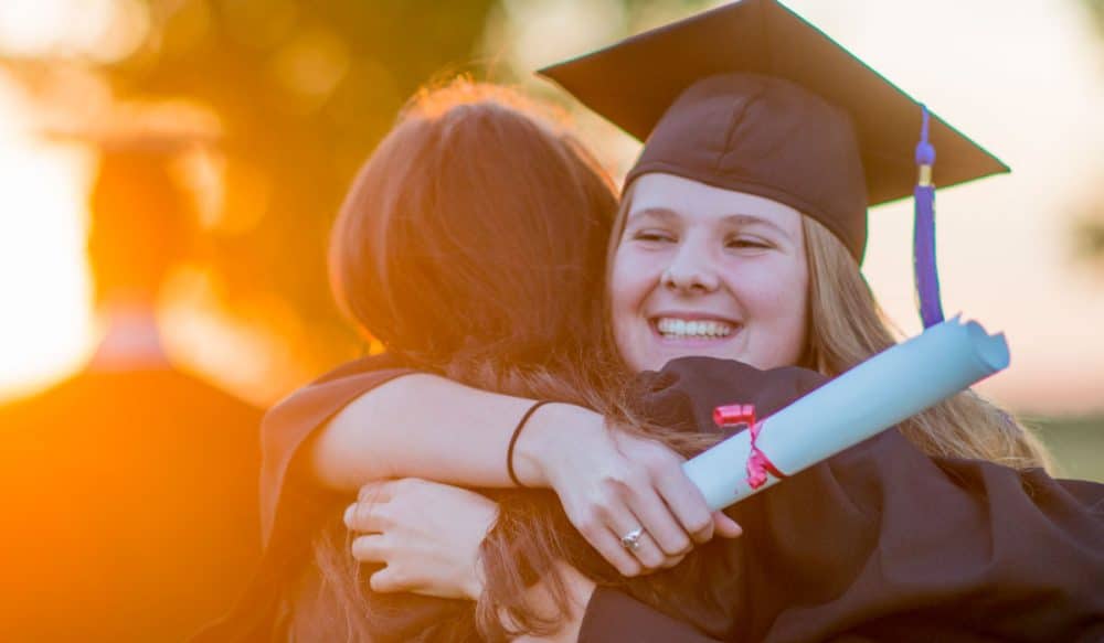 A woman with a graduation cap on hugs another woman