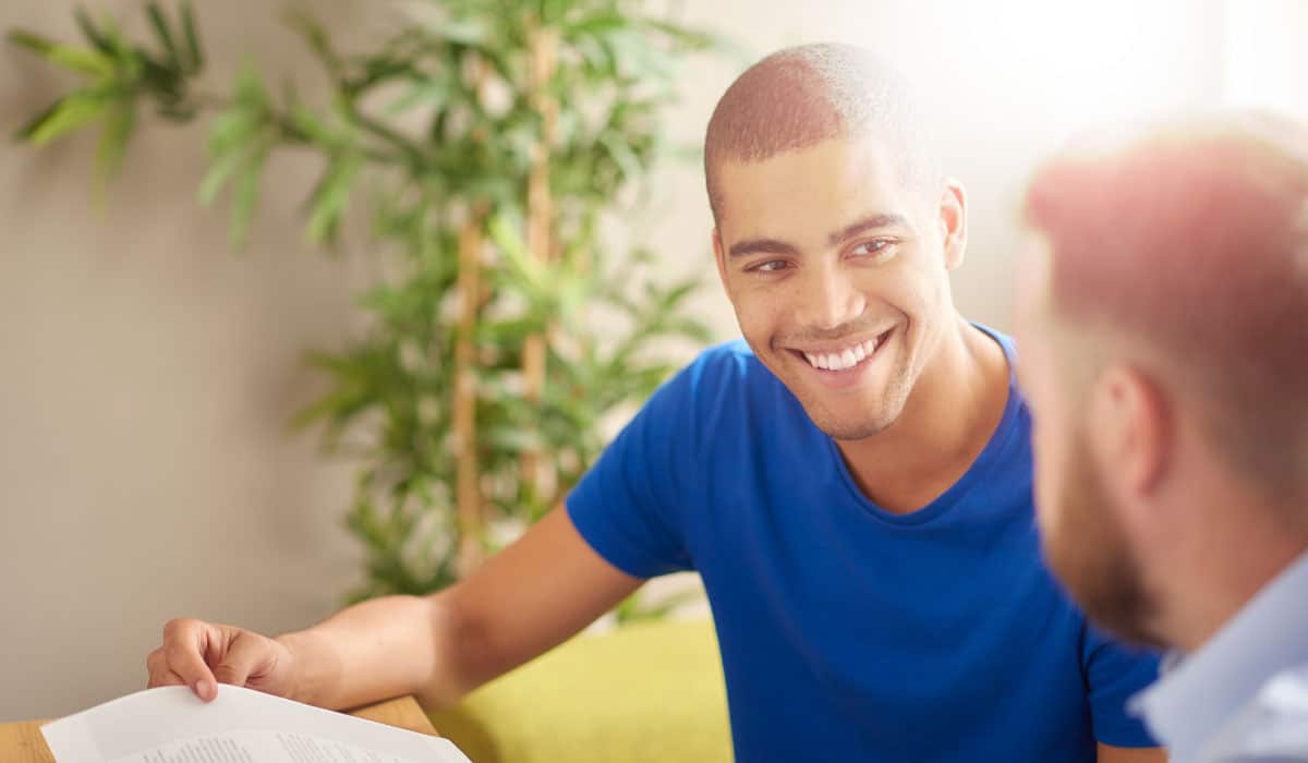 two men looking at each other and smiling while holding paperwork