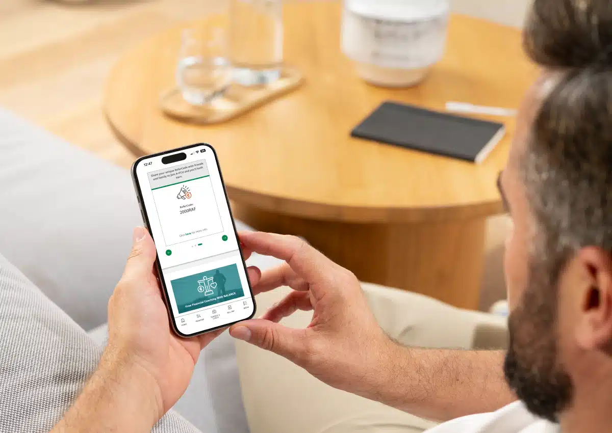 Person holding a smartphone displaying a financial app in a living room setting.