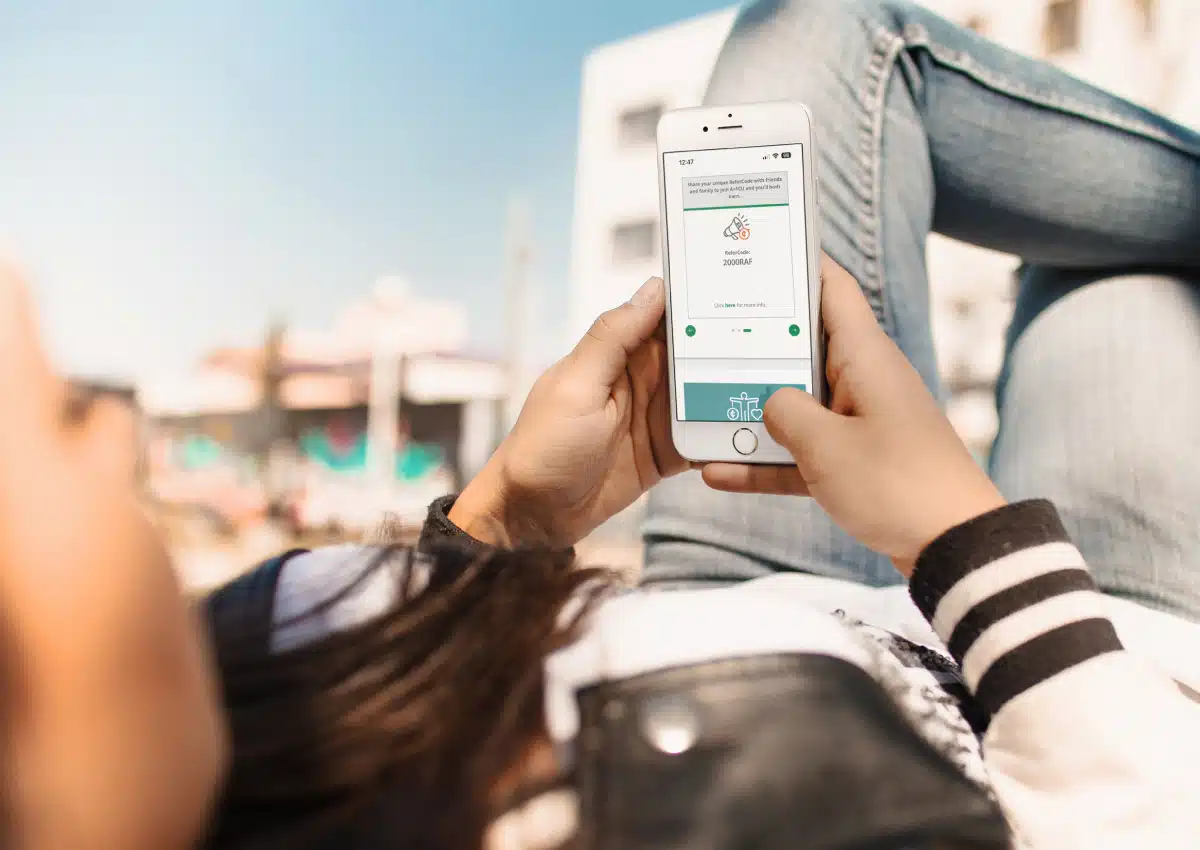 Person lounging outdoors, using a smartphone to view an app screen.