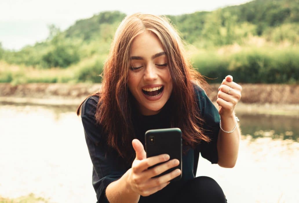 Woman holds mobile phone while laughing and celebrating