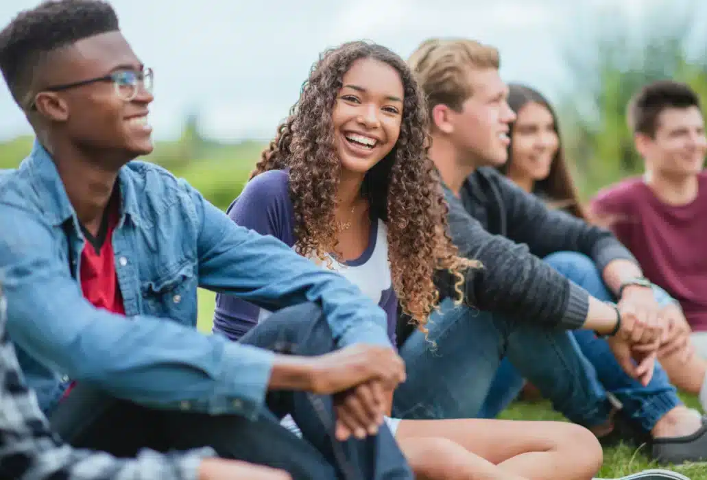 Diverse group of smiling friends sitting on the grass outdoors, enjoying a sunny day.