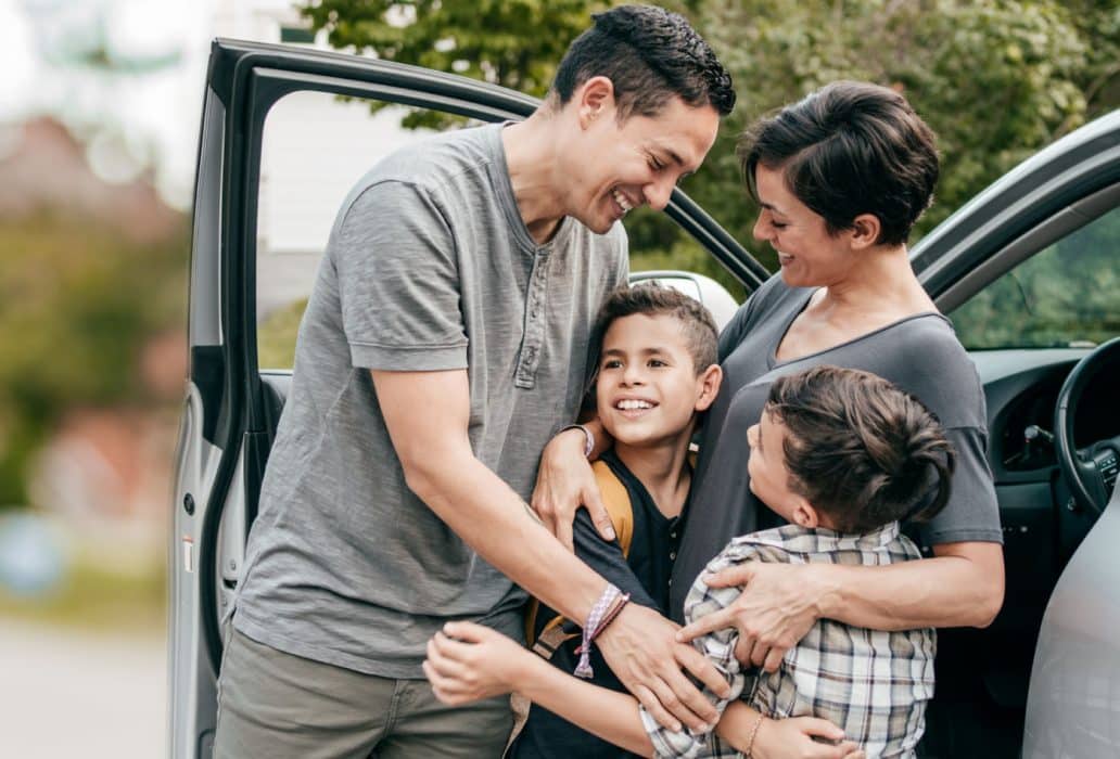 A family hugs beside an open car door.
