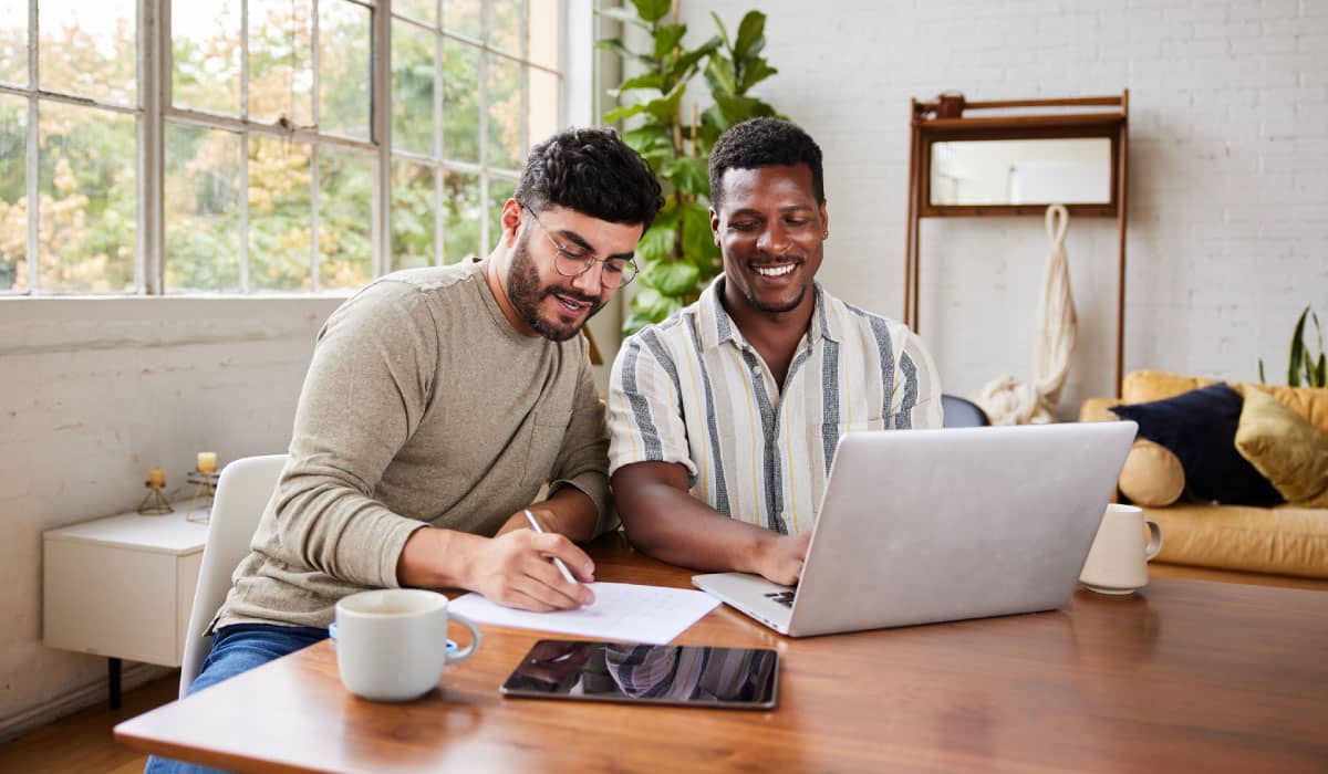 Two men sit at a table and use a laptop