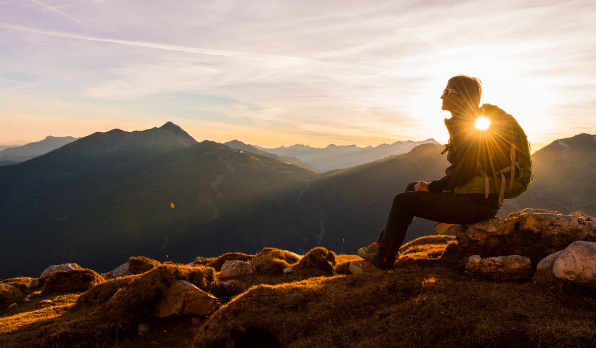 A woman sitting on top of a mountain. She is wearing a hiking backpack.