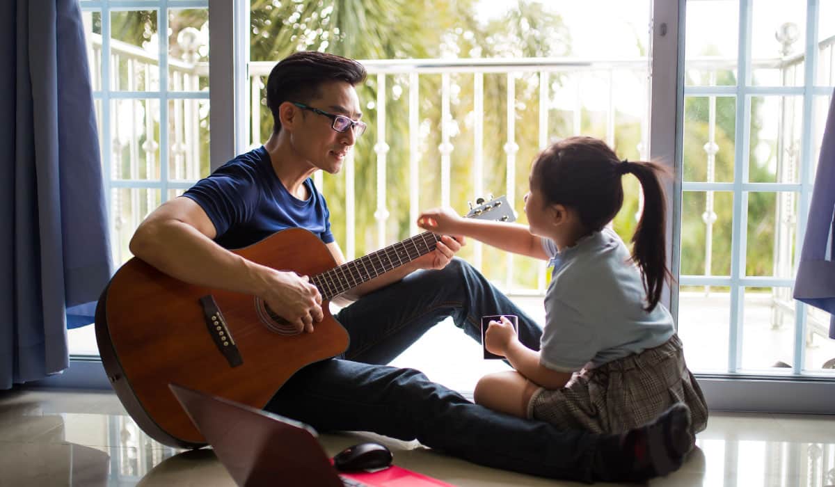 A man holding a guitar while a young girl reaches out to strum it.