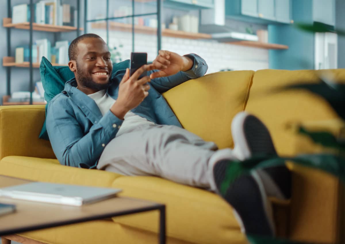 A man laying on a couch and using a cell phone.