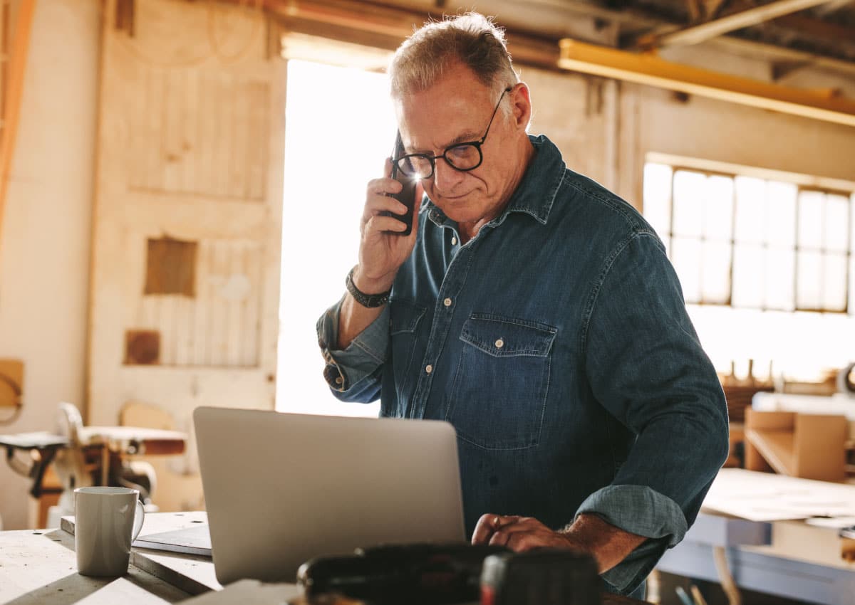 A man on a phone while using an open laptop.