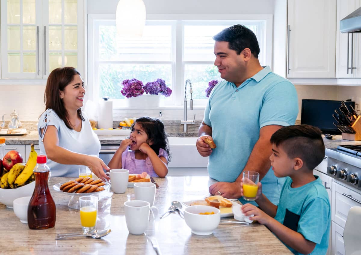 A family standing in a kitchen and eating breakfast.