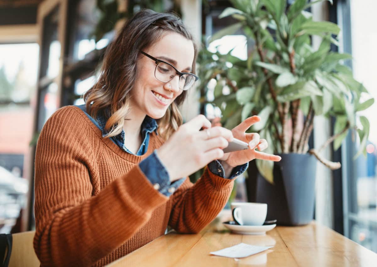 A woman sitting in a coffee shop and depositing a check by using her cell phone.